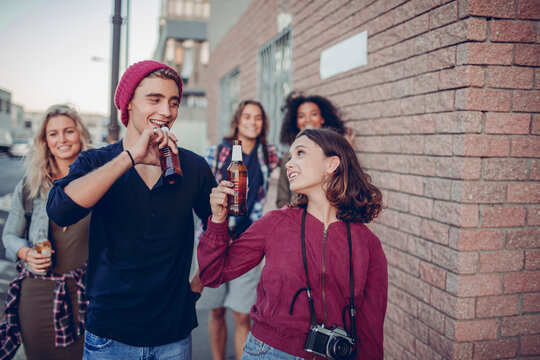 Young adults drinking beer while walking on a city street