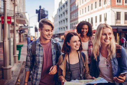 Smiling young friends sightseeing with map on urban street
