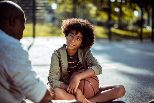 Teen boy talking with mentor on outdoor basketball court