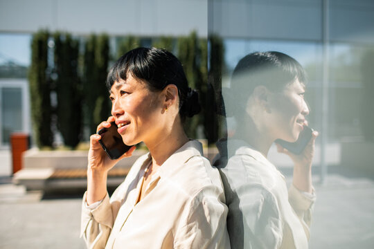 Smiling businesswoman talking on smartphone outside glass office building