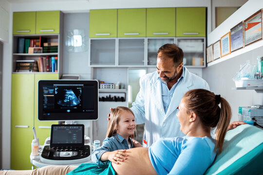 Obstetrician performing prenatal ultrasound for pregnant mother and daughter in clinic