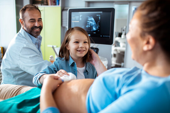 Doctor performing prenatal ultrasound with big sister watching in clinic