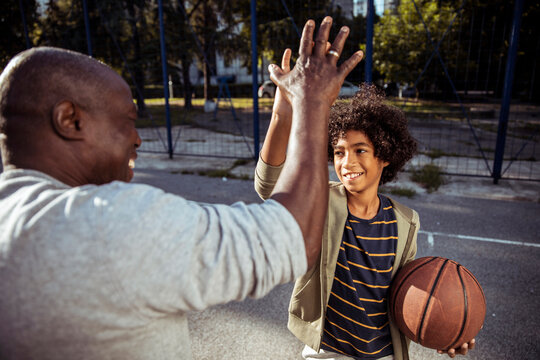 Father and son high five after basketball practice on outdoor court