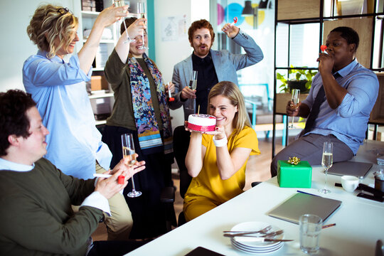 Coworkers celebrate birthday with cake in modern office