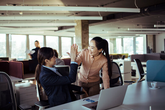 Two businesswomen high five in modern open-plan office