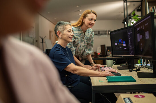 Two women collaborating on design at dual monitors in modern office