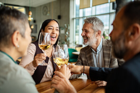 Happy friends toasting white wine at modern restaurant