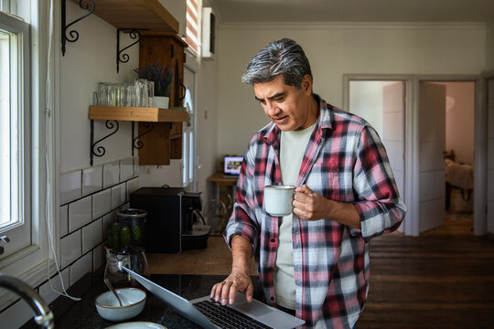 Middle-aged man working on laptop in home kitchen