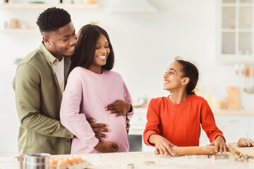 Obraz premium A family spends time together in a kitchen, preparing food and enjoying each other's company. The parents smile as their daughter rolls out dough and shares happy moments.