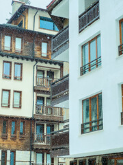 Fototapeta premium Snow falls on buildings in a mountain town with wooden and modern design features during winter season