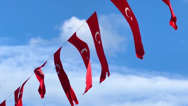 Multiple Turkish flags hanging on a rope and waving in the wind against a blue sky with white clouds. National identity, patriotism, and public decoration concept