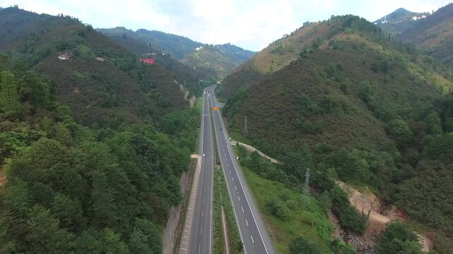 Aerial view of highway roads running through forested mountain valley landscape scenery. Dual carriageway cuts green hills as an orman yolu double road connecting rural terrain.