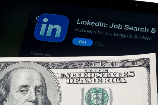 LinkedIn logo and App Store page on iPad in Apple Liquid Glass iOS 26 design beside US dollar note. Stafford, United Kingdom, April 13, 2026.