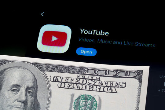 YouTube app on iPad showing Apple Liquid Glass redesign and iOS 26 App Store look beside US dollar banknote. Stafford, United Kingdom, April 13, 2026.