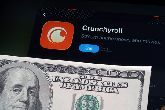 Crunchyroll logo and App Store page on iPad in Apple Liquid Glass iOS 26 design beside US dollar note. Stafford, United Kingdom, April 13, 2026.