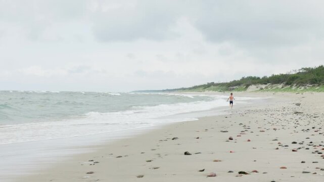 A solitary runner jogs steadily along a serene beach, surrounded by gentle waves and vibrant lush greenery all around