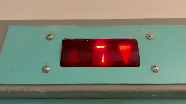 White panel, Red Passenger Elevator Display Close-up of the number 5 glowing red. A Small Plaque with an Inscription.