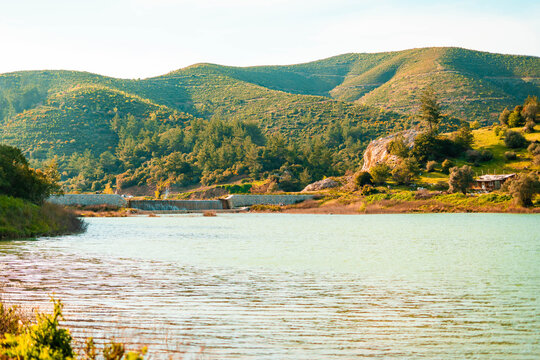 Serene lake with rolling green hills and a small dam in the distance
