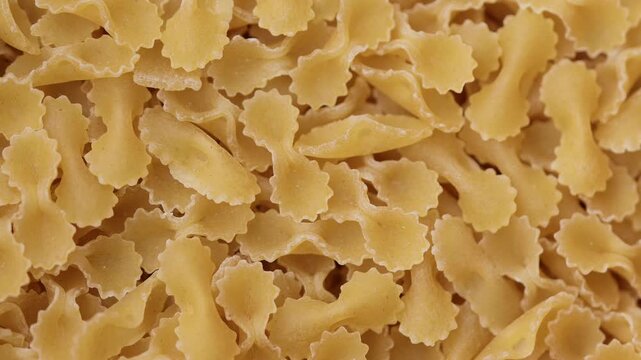 Close up texture of uncooked farfalle pasta with detailed shapes and natural yellow color italian food ingredient background for cooking and cuisine concepts. 