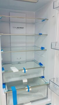 Closeup new refrigerator interior glass shelves and crisper drawers with protective blue tape, pristine empty compartments.