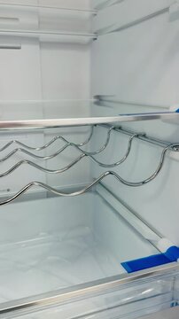 Empty refrigerator wine rack closeup showing glass shelves and wave shaped bottle holder, crisp crisper compartment, No Frost label.