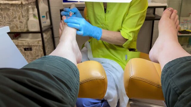 Doctor specializing in foot and nail diseases who treats gloved nails in clinical setting, removes the nail plate with an electric drill, pays special attention to diabetic foot care and sterility.