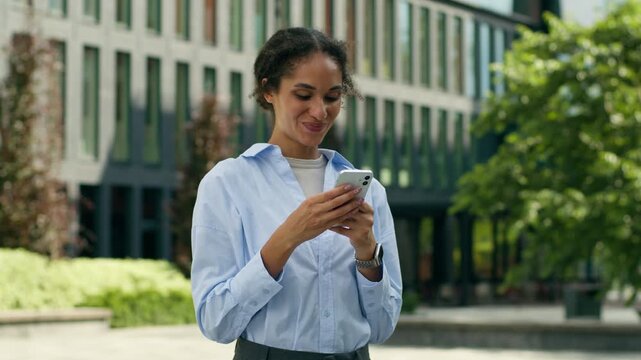 Smiling African American business woman celebrating victory mobile phone in city happy winner champion female entrepreneur rejoicing good news success yes gesture prize downtown businesswoman triumph