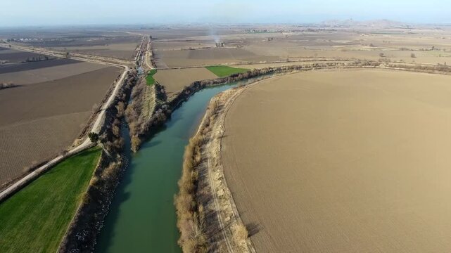 Aerial view shows irrigation canal merging with Yangtze River across flat alluvial plain in China. Wide perspective reveals brown empty fields engineered waterways and vast agricultural land.
