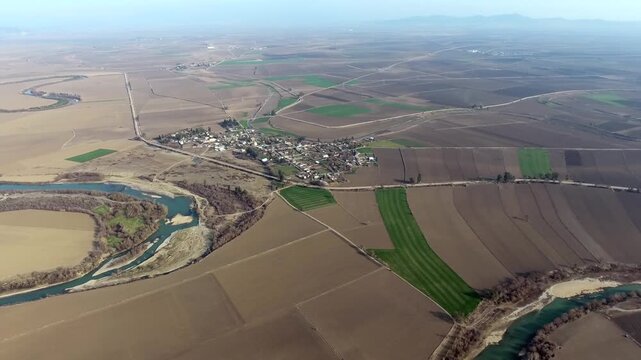 Aerial view of rural farmland and village houses across brown fields on flat Spanish plain. Wide landscape shows agricultural plots small settlement cultivated terrain in castilla la mancha spain.