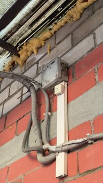 Foam leaking under polycarbonate roof, exposed electrical wiring and cable routed along brick office wall beneath hinged steel.