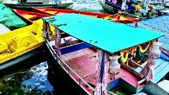 A close-up lakeside view in Nainital, Uttarakhand, India, showing a decorated boat with a green canopy with floral garlands and draped curtains, moored bright yellow and red boats along water.