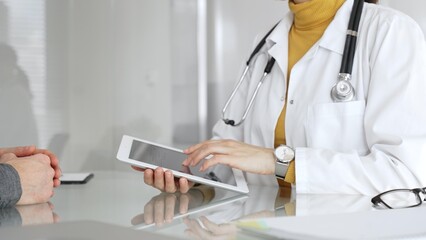 Doctor consulting patient using digital tablet, explaining medical information during modern...