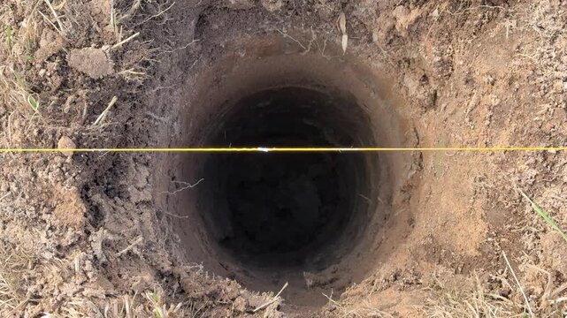 Deep round holes for fence posts, surveyor marking layout with yellow string, landscaper clearing loose soil, contractor preparing.