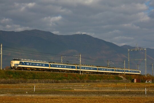 山並みをバックに田園地帯を快走する寝台特急形電車