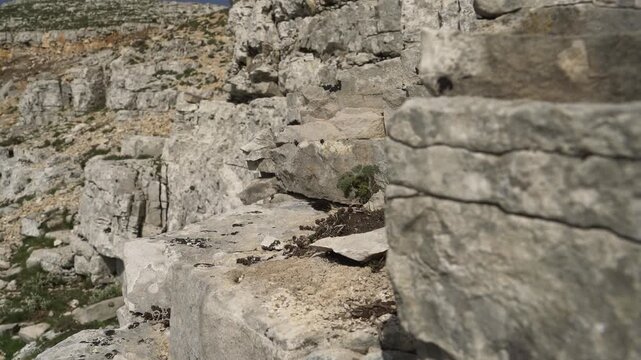 White gray limestone bedrock forms a stepped tectonic landscape with strong mineral relief. Pale calcite layers, rocky shelves, and uplifted ground create striking geologic texture outdoors.