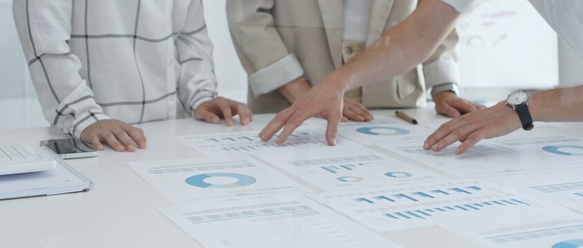 Professional team reviewing financial data, collaborating on charts and graphs in office, pointing toward key statistics during strategic planning session. Business people concept