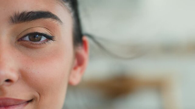 Close up half face Indian woman looking at camera smiling eye makeup indoor feminine female Arabian Latina girl with eyeliner mascara eyesight health beauty positive happy human portrait cropped view