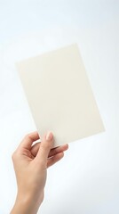 Obraz premium Female hand holding blank cream colored paper sheets against white background isolated for mockup design and presentation templates.