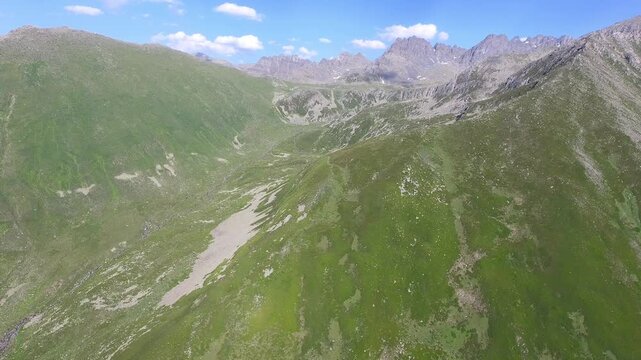 Aerial u shaped valley with stream and green meadows spans treeless alpine terrain. Glacial basin, grassy slopes, broad uplands define a remote highland landscape clear light.