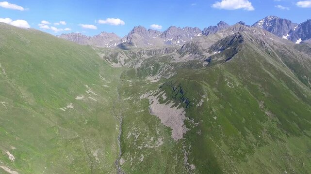 Aerial Ladakh India u shaped valley with green meadows spreads across treeless alpine highlands. Glacial basin, grassy slopes, and rugged relief create a remote Himalayan landscape under big skies.