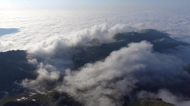 Aerial Peruvian Andes mountain peaks rise above clouds with rugged ridges and high altitude drama. Misty layers, vapor flow, elevated relief create striking atmospheric scenery across remote ranges.