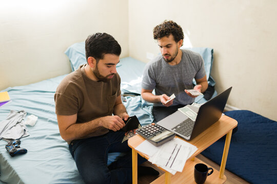 Latin men budgeting and calculating finances, managing household bills while counting money in their first apartment