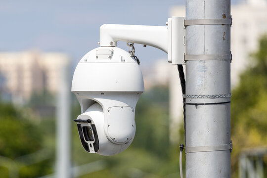 Modern white outdoor PTZ security camera mounted on a metal pole for city surveillance, high-tech dome CCTV system for public safety and monitoring in urban area