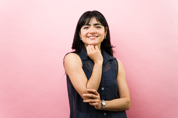 Obraz premium Smiling latina woman posing in studio against pink background, expressing happiness, confidence, and positive emotions