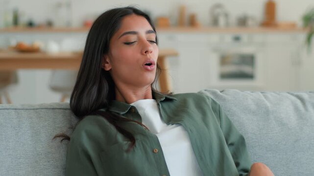Upset overheated Indian woman at home waving hand trying cool down sweating hot frustrated Arabian Muslim female girl suffer high temperature discomfort broken air conditioner climate control indoors 