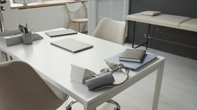 High angle of blood pressure monitor, documents and notebook, laptop and digital tablet on white table in modern minimalist doctors office interior