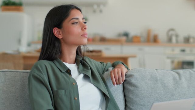 Serious concentrated Indian woman working studying online typing laptop at home looking away thinking pondering Arabian female girl author writing PC computer inspiration solution focused indoors