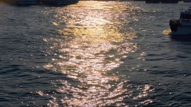 Silhouette of a passenger ferry crossing the Golden Horn at sunset in Istanbul. Glowing sun reflection, ripples on water and a bright sun trail create a dramatic evening scene