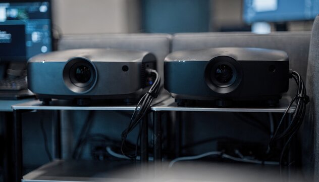 Inside a twin booth setup a medium shot captures dual projectors side by side racks and wiring gently out of focus creating a dynamic tech atmosphere.