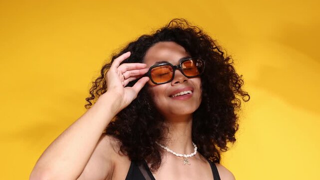 Woman in black swimsuit and sunglasses on orange background